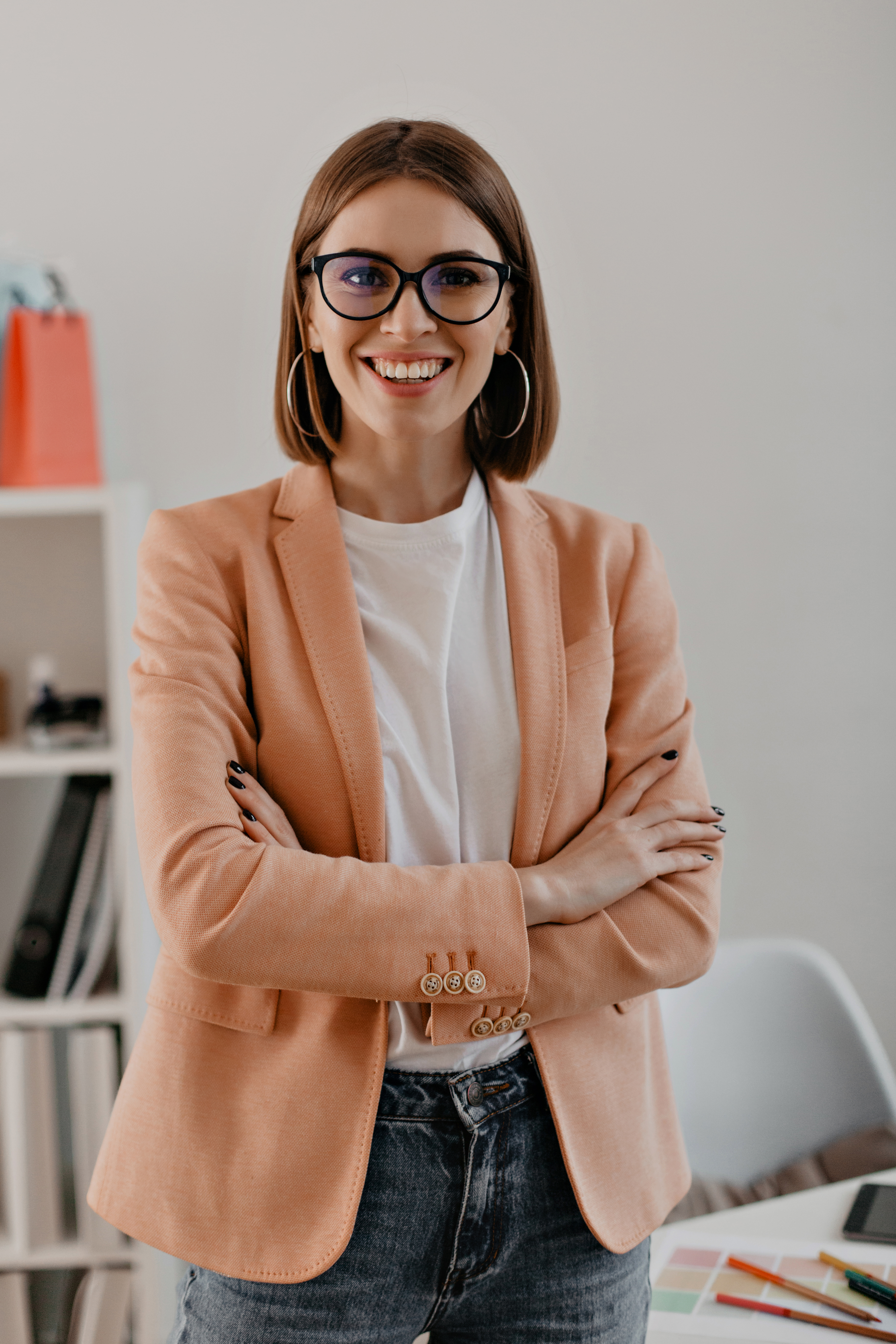 Close-up portrait of smiling short-haired business woman in white t-shirt posing with arms crossed in white office